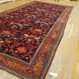 Large navy and rust-red floral patterned rug with multiple borders rests on light wooden planks.