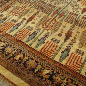 Low pile rug with a tan field and repeating tribal motifs, bordered in navy blue, sitting on wood plank flooring.