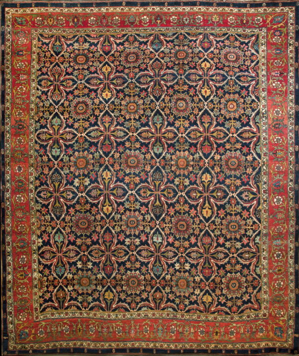 Dark blue rug displaying a repeating multicolored floral lattice design and a wide red botanical border.