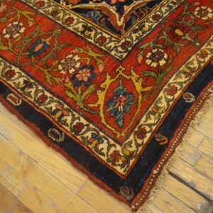 Ornate red, navy, and cream floral rug border resting on worn, light-colored wooden planks.