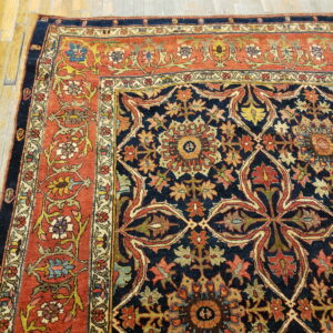 Close-up of a dark navy and rust traditional rug featuring intricate floral patterns on a wood floor.