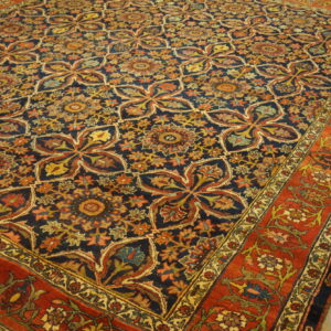 Dark blue rug with repeating medallions and a red floral border rests on light wood flooring.