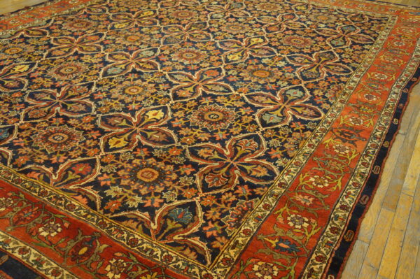 Dark blue rug with repeating medallions and a red floral border rests on light wood flooring.