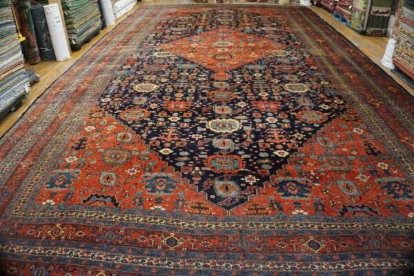Navy blue and rust traditional patterned rug with geometric motifs displayed on hardwood surrounded by rug stacks.