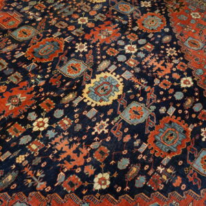 Close-up of a low-pile rug with a navy blue field, featuring intricate red, teal, and gold geometric medallions.
