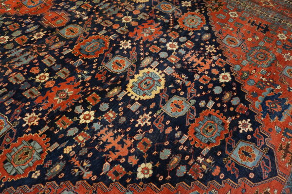 Close-up of a low-pile rug with a navy blue field, featuring intricate red, teal, and gold geometric medallions.