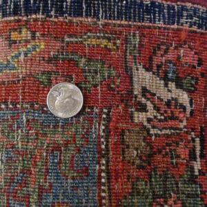 Low-pile rug segment featuring densely woven red, navy, and green geometric patterns, with a quarter for scale.
