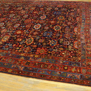 Large dark blue rug with detailed red, rust, and teal patterns, laid flat on light wooden planks.