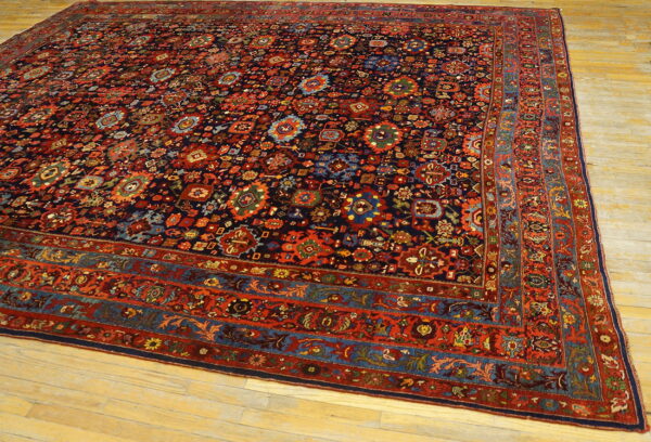 Large dark blue rug with detailed red, rust, and teal patterns, laid flat on light wooden planks.