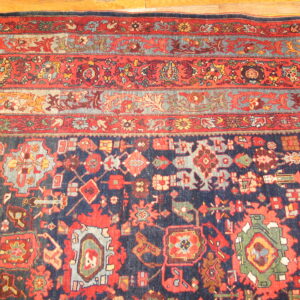Low-pile rug in navy and red with dense geometric patterns and ornate floral borders on wood floor.