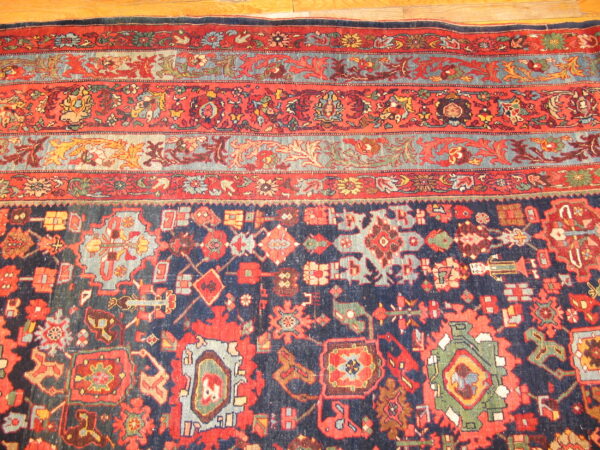 Low-pile rug in navy and red with dense geometric patterns and ornate floral borders on wood floor.