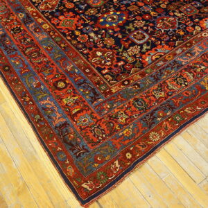 Intricate red and navy traditional rug border and field corner lying on faded blonde wood planks.