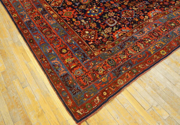 Intricate red and navy traditional rug border and field corner lying on faded blonde wood planks.