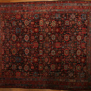 Oversize dark rug with intricate red, blue, and green tribal motifs on light wooden flooring.
