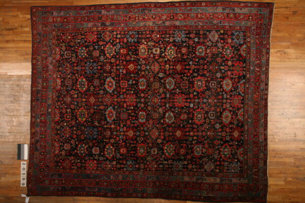 Oversize dark rug with intricate red, blue, and green tribal motifs on light wooden flooring.