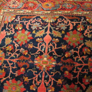 Intricate floral rug design featuring a dark blue field framed by a wide red decorative border.