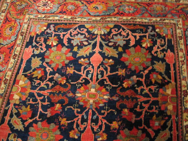 Intricate floral rug design featuring a dark blue field framed by a wide red decorative border.