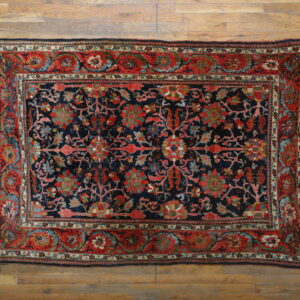 Ornate navy rug with red, blue, and green floral motifs rests on light wood planks.