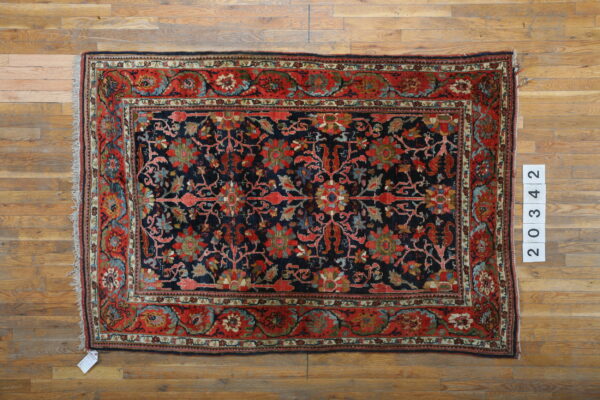 Ornate navy rug with red, blue, and green floral motifs rests on light wood planks.