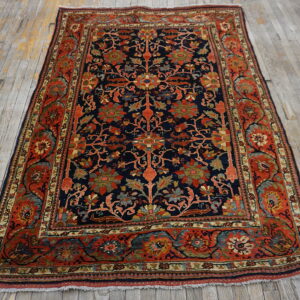 A navy and red traditional floral rug with dense patterns rests on distressed gray wood plank flooring.