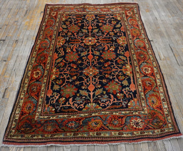 A navy and red traditional floral rug with dense patterns rests on distressed gray wood plank flooring.