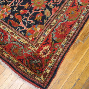 Traditional rug corner featuring a navy field and red border with multi-colored floral designs on wood planks.