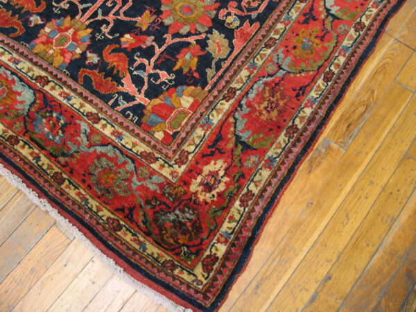 Traditional rug corner featuring a navy field and red border with multi-colored floral designs on wood planks.