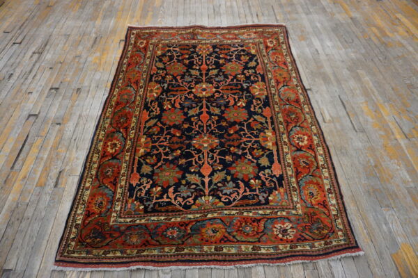 Low-pile rug featuring a navy floral field and wide red border on worn gray and yellow wooden planks.