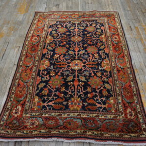 Ornate navy blue rug with a red floral border sits on distressed gray and yellow plank flooring.