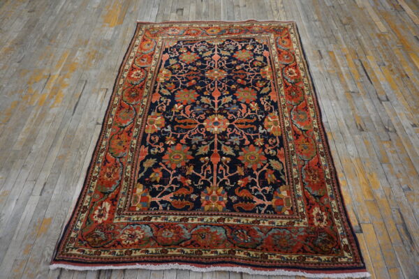 Ornate navy blue rug with a red floral border sits on distressed gray and yellow plank flooring.
