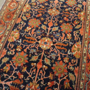 Intricate navy and rust floral rug with multi-colored accents rests on light gray hardwood flooring.