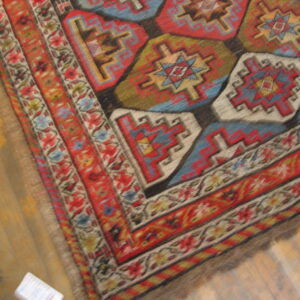 Red, blue, green, and cream geometric rug with a detailed border rests on golden wood planks.