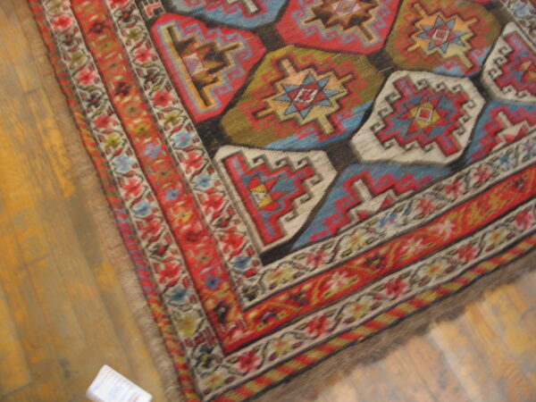 Red, blue, green, and cream geometric rug with a detailed border rests on golden wood planks.