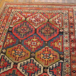 Low-pile rug with a complex red and blue geometric pattern and floral border on hardwood flooring.