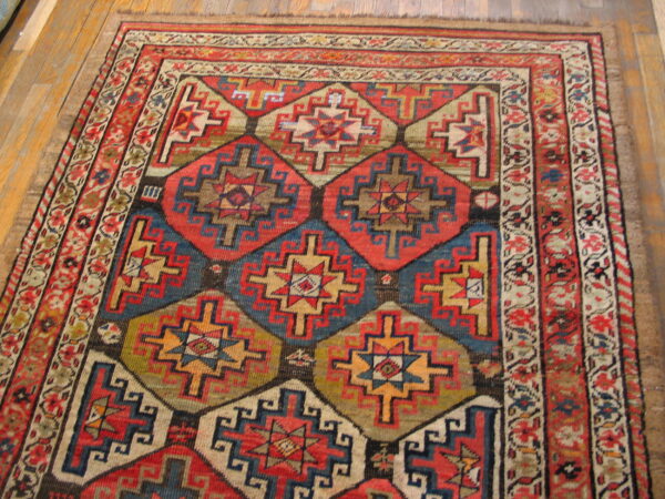 Low-pile rug with a complex red and blue geometric pattern and floral border on hardwood flooring.