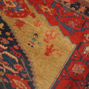 Woven rug detail showing a tan field with stylized figures bordered by red and navy geometric motifs.