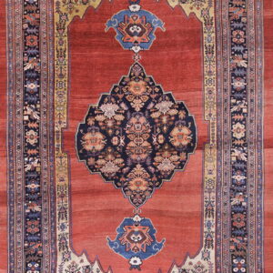 Rust-red rug with a navy medallion and stylized borders, including cream and gold arch patterns.