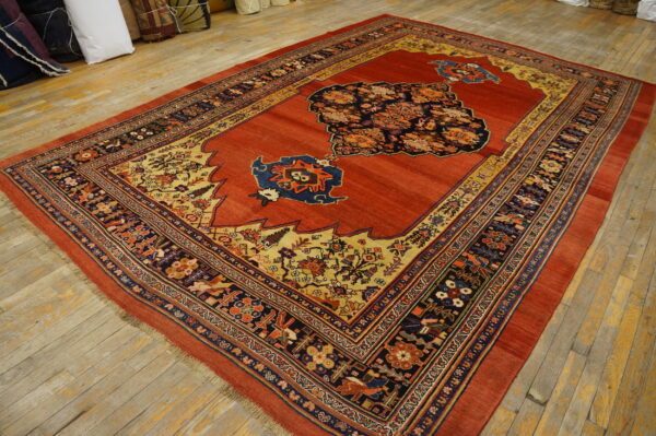 Red rug with an elaborate multicolored medallion and patterned borders covers light-toned wood flooring.