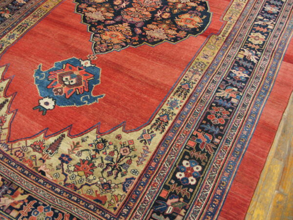 Detail view of a coral red rug featuring intricate navy, beige, and blue traditional patterning on wood flooring.