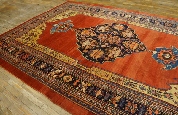 Terracotta and navy rug with an ornate central medallion and multicolored borders sits on light wooden flooring.