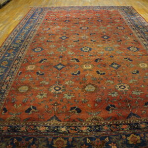 Oversized rust rug with detailed blue and green scrolling floral patterns on light wood flooring.