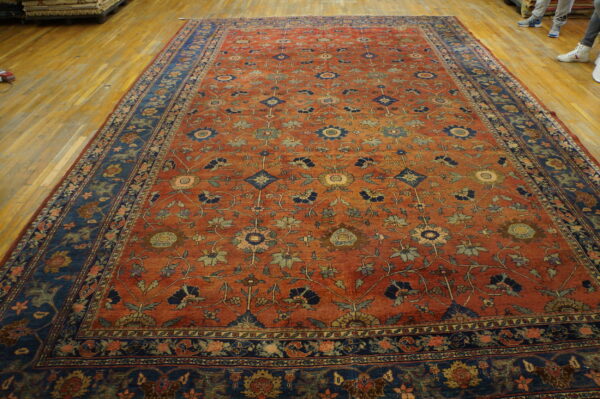 Oversized rust rug with detailed blue and green scrolling floral patterns on light wood flooring.