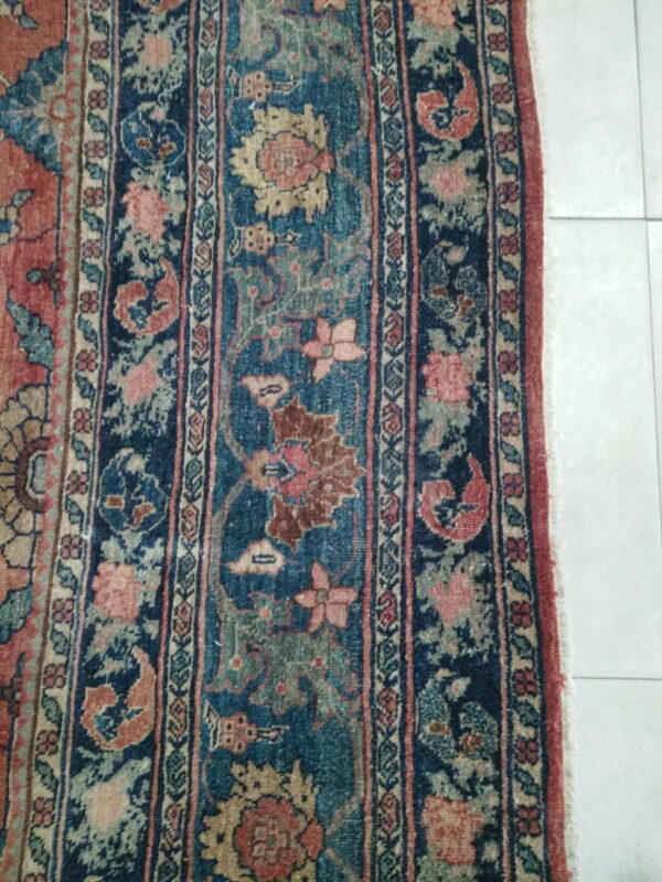 Worn traditional rug with red, blue, and tan botanical patterns rests on light square tiles.