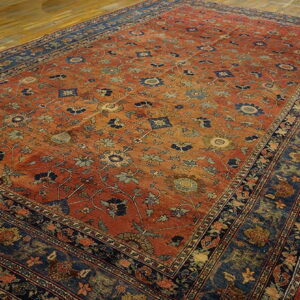 Rust and blue traditional rug with a detailed floral pattern on worn wood floors.
