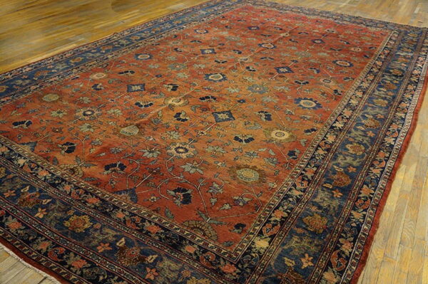 Rust and blue traditional rug with a detailed floral pattern on worn wood floors.