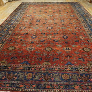 Low-pile red rug with detailed blue floral designs and wide blue borders displayed on wood flooring.