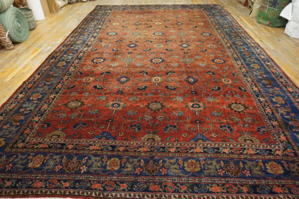 Low-pile red rug with detailed blue floral designs and wide blue borders displayed on wood flooring.