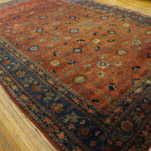 Ornate floral rug in red-orange and navy blue on distressed wide plank hardwood floors.