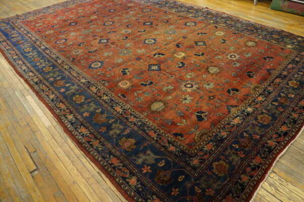Ornate floral rug in red-orange and navy blue on distressed wide plank hardwood floors.