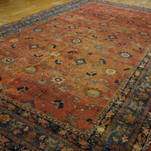Large rusty red rug with an all-over floral pattern and a wide navy and blue border on wood floors.